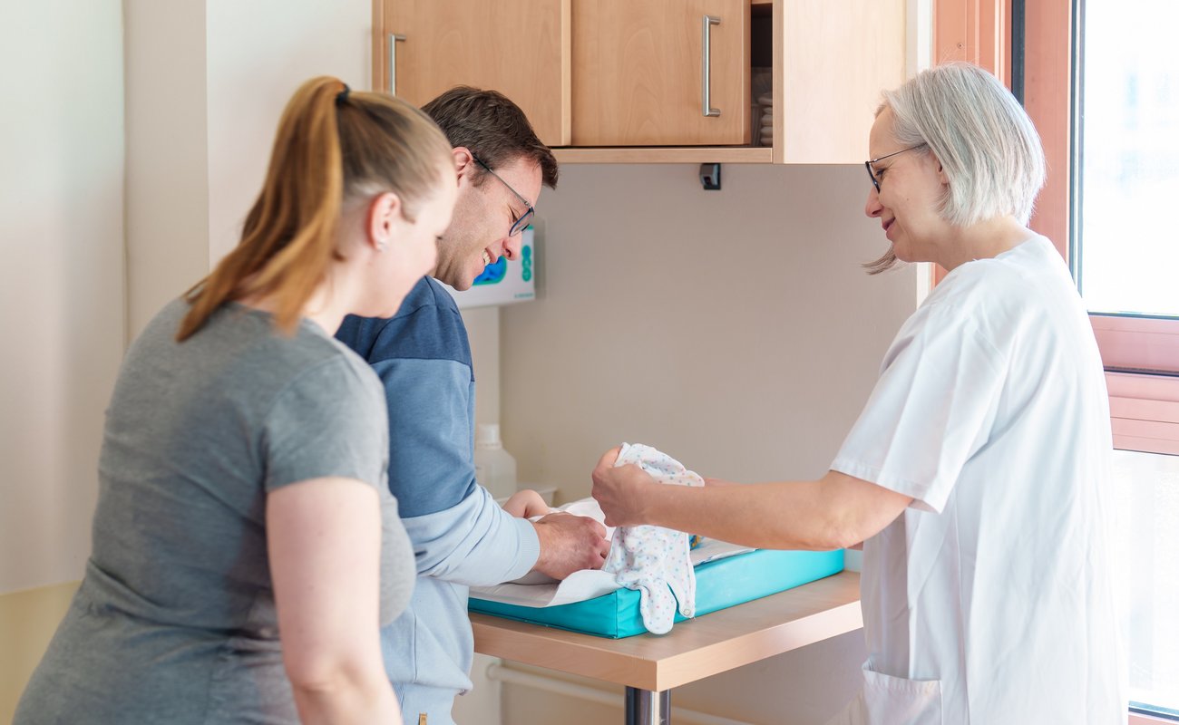 Eltern mit Hebamme am Wickeltisch.