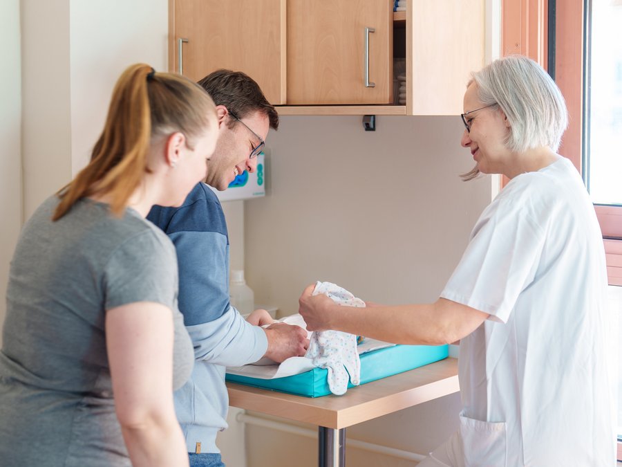 Eltern mit Hebamme am Wickeltisch.