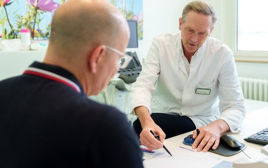 Prof. Gröne erklärt Patienten mit Unterstützung einer Zeichnung.
