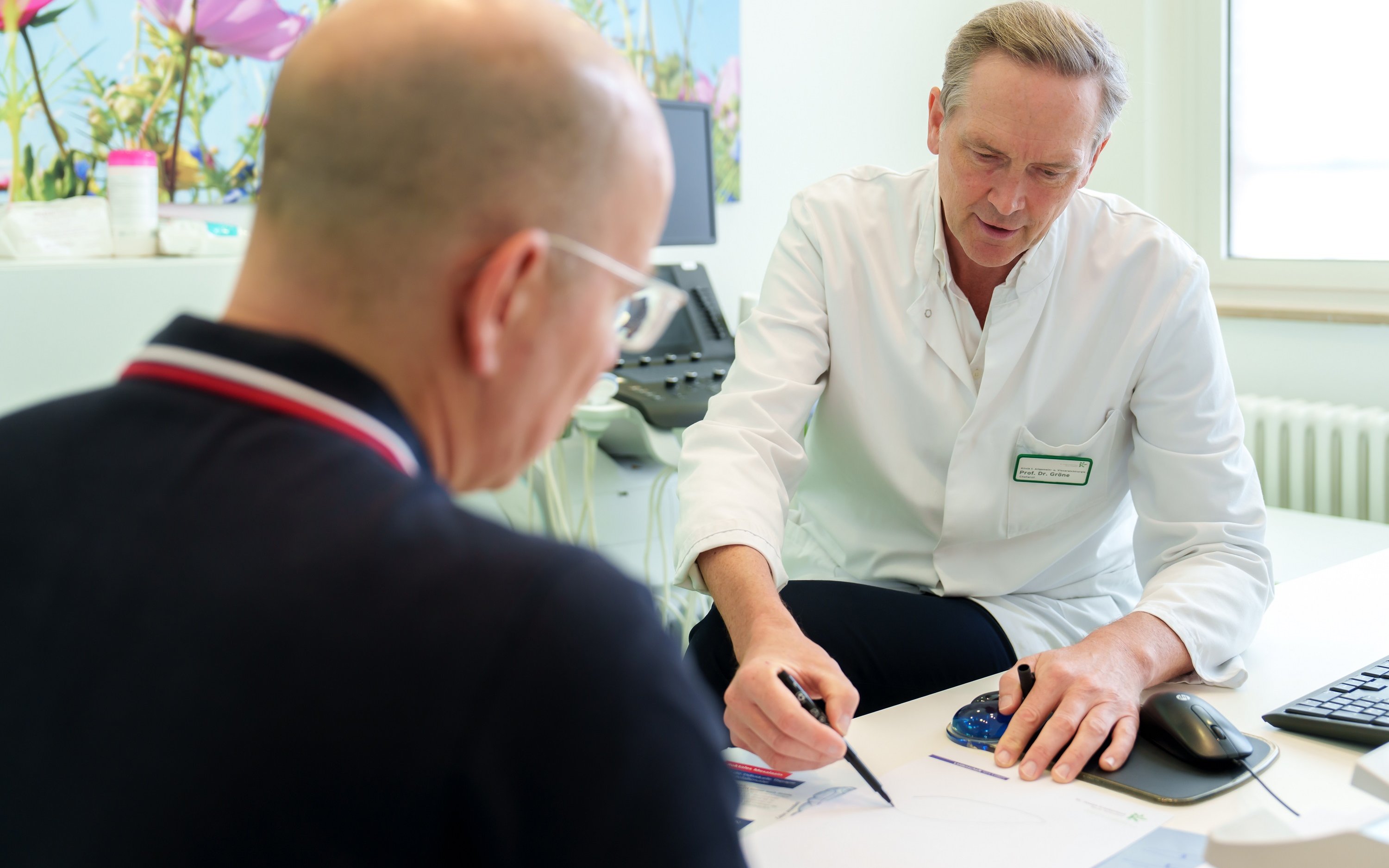 Prof. Gröne erklärt Patienten mit Unterstützung einer Zeichnung.